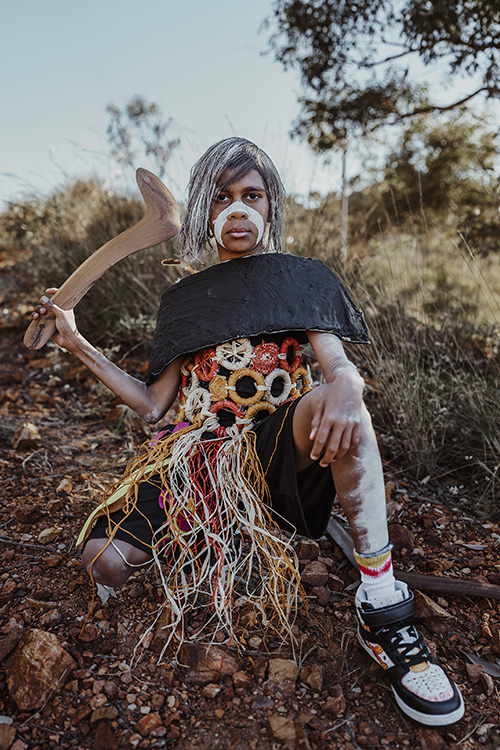 Photo of the student wearing their art piece and shoes with white paint across their face.