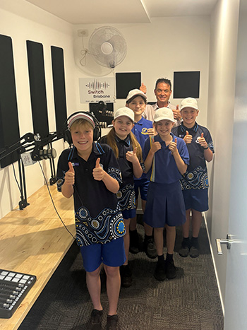 A group of happy students and a staff member posing for a group photo in a studio.